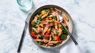 Pasta met tonijn, groenten en saus op een bord.