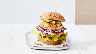Kipburger met avocado, sla, paprika en kool op een meergranenbroodje, gepresenteerd op een bord.
