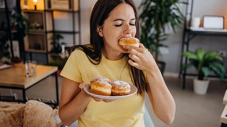 Vrouw in een gele trui houdt een bord met donuts vast in een gezellige kamer.