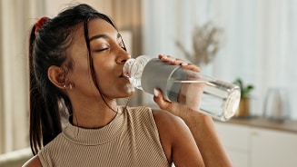 Vrouw drinkt water uit fles in woonkamer.