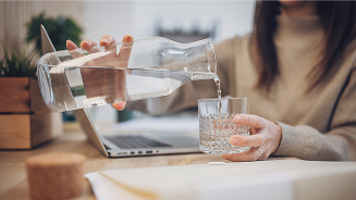 Persoon schenkt water in een glas naast een laptop op een bureau