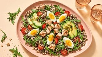 Quinoasalade met stukjes kipfilet, gekookte eieren, avocado, cherrytomaten en rucola op een roze bord.