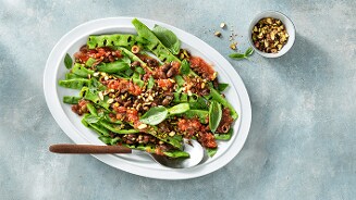 Gerecht van snijbonen met tomatensaus, olijven en pistachenoten op een witte schaal.