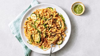 Spaghetti met kikkererwten en gegrilde courgette, geserveerd met een kommetje groene pesto.