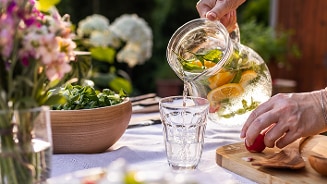 Schenken van citroen- en muntinfused water op een zomerse tafel.