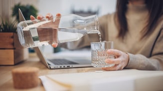 Iemand schenkt water in een glas naast een laptop
