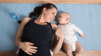 Moeder en baby liggend op een blauwe yogamat met een waterfles in de buurt.