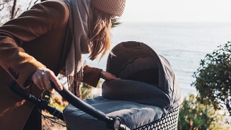 Vrouw met kinderwagen wandelt langs de kust.