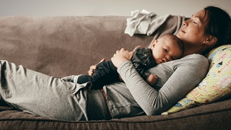 Moeder liggend op een bank die een baby in haar armen houdt.