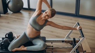 Zwangere vrouw in sportkleding doet Pilates-oefeningen op een reformer apparaat.