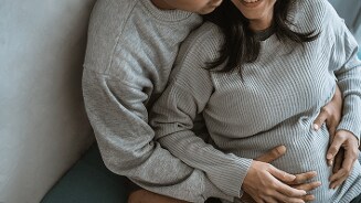 Zwangere vrouw die liefdevol omarmd wordt door haar partner.