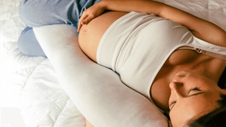 Zwangere vrouw liggend op een bed met een zwangerschapskussen.