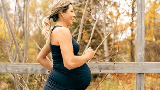 Zwangere vrouw die buiten sportieve kleding draagt en wandelt in een herfstlandschap.