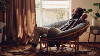 Persoon ontspannen in een rotan stoel in een sfeervol ingerichte woonkamer met tapijt en planten