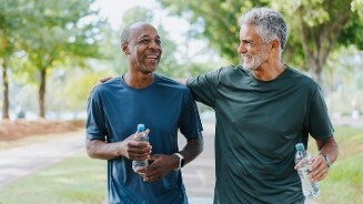 Twee mannen in sportkleding wandelen samen buiten in een park en houden flesjes water vast