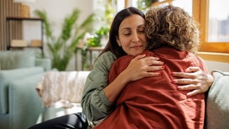 Twee mensen die elkaar een knuffel geven op een bank in een woonkamer met veel natuurlijk licht