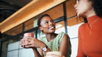 Vrouw in groene top drinkt koffie en praat met iemand in een gezellige moderne omgeving