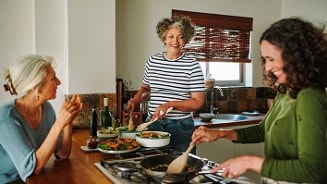 Drie mensen bereiden samen een maaltijd in een huiselijke keuken, met verschillende pannen en borden met eten op het aanrecht.