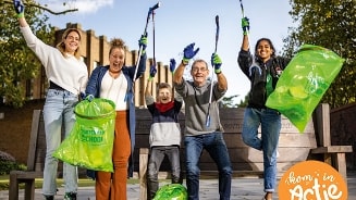 Groep mensen met afvalknijpers en groene vuilniszakken tijdens een schoonmaakactie in een park, organisatie 'Ik ben in Actie'.