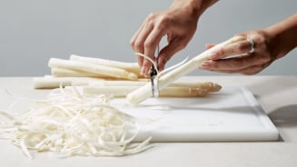Handen schillen witte asperges op een snijplank.