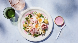 Bord met salade van ham, asperges, gekookte eieren, krieltjes, doperwten en roze dressing, naast een groene en roze drank.