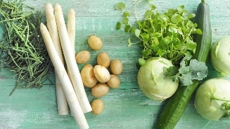 Verse groenten op een groene houten achtergrond, waaronder witte asperges, kruimige aardappelen, komkommer, koolrabi, zeekraal en waterkers.
