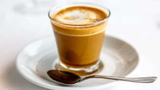 Glas met vers gezette espresso op een schotel met een lepel.