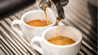 Twee kopjes vers gezette espresso onder een espressomachine.
