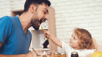 Vader en kind aan tafel met ontbijtgranen en potjes jam
