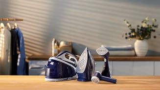 Strijkijzers en kledingstomer in een moderne wasruimte, met kleding op een rek en een vaas met bloemen op de achtergrond.