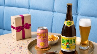 Blik Mannenliefde bier en fles La chouffe Blonde speciaalbier op een rond dienblad met een glas bier, een bakje chips en een cadeau met roze strik op de achtergrond.