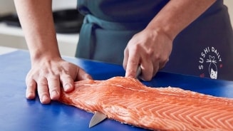 Een zalmfilet wordt gesneden door een medewerker van Sushi Daily.