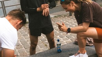 Drie sporters op een stoep, met een flesje AA Drink isotone sportdrank op de voorgrond