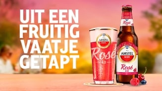 Amstel Radler Rosé 0.0% bierfles en glas met de tekst "Uit een fruitig vaatje getapt" op een zomerse achtergrond.