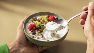 Kom yoghurt met muesli, kiwi, blauwe bessen en frambozen, vastgehouden in een hand met een lepel