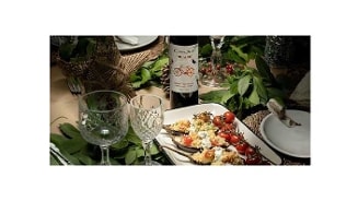 Een sfeervol gedekte tafel met een fles Cono Sur Bicicleta Orgánica wijn, kristallen wijnglazen, en een bord gevuld met gevulde aubergines en cherrytomaatjes.