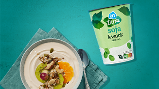 Kom ontbijt met AH Terra soja kwark, ongezoet, geserveerd met vers fruit en noten. De verpakking van AH Terra soja kwark staat ernaast op een blauwe achtergrond.