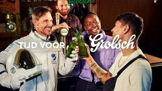 Groep mensen die proosten met Grolsch flesjes in een bar, met een persoon in astronautenpak.