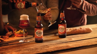 Grolsch Herfstbier 0.0 flesjes op houten tafel, met borrelhapjes zoals stokbrood en olijven, mensen schenken bier in glazen