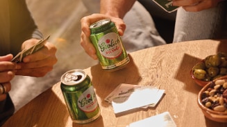 Vrienden spelen een kaartspel aan een houten tafel met blikjes Grolsch pilsner, een schaaltje olijven en een schaaltje noten.