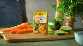 Pak Maggi Honey Mustard saus op een houten snijplank, omringd door wortels, komkommer en verse peterselie