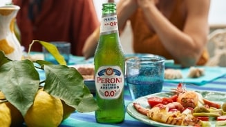 Peroni Nastro Azzurro 0.0% fles op een tafel met citroenen en een bord antipasti.