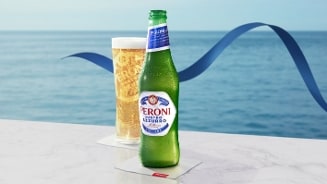 Fles en glas Peroni Nastro Azzurro bier met zeezicht op de achtergrond.