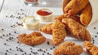 Gefrituurde kipnuggets met zwarte peperkorrels en sausjes op een houten tafel.