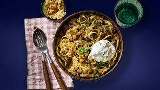 Pasta met champignons, kikkererwten, Parmezaanse kaas en een gepocheerd ei, geserveerd in een kom op een blauw oppervlak met bestek op een geruit servet.