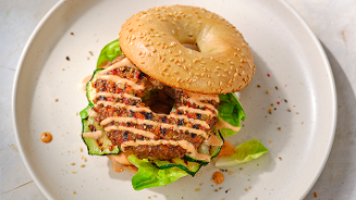 Bagelburger met een quinoa veggieburger, sla en een saus, geserveerd op een wit bord.