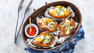 Gepofte zoete aardappelen met kruiden en feta in een ovenschaal, geserveerd met een schaaltje saus.