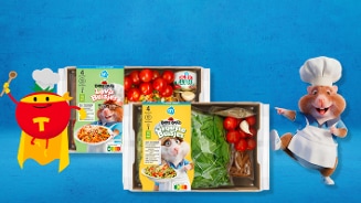 Twee maaltijdpakketten van Albert Heijn met verse groenten, cherrytomaten en pasta, afgebeeld met een getekende tomaat in superheldenkostuum en een hamster in een kokspak op een blauwe achtergrond.