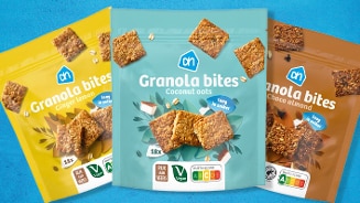 Drie zakken Albert Heijn Granola bites in de smaken Ginger Lemon, Coconut oats en Choco almond, uitgestald tegen een blauwe achtergrond.