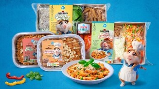 Verschillende Tommie's Tomat maaltijdboxen en -schalen van Albert Heijn, waaronder Groene Buistjes, Lava Buistjes, Bolo Boogjes en Magische Macaroni, uitgestald naast een schaal met pasta, omringd door kleurrijke ingrediënten, en een getekende hamsterchef.